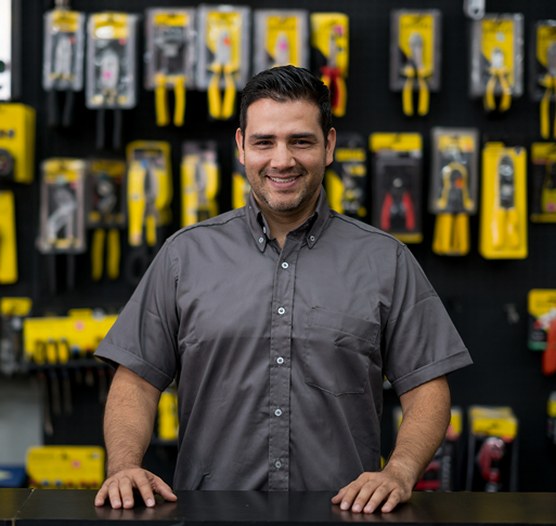 Vendedor sonriente de una ferretería, con una pared de herramientas detrás