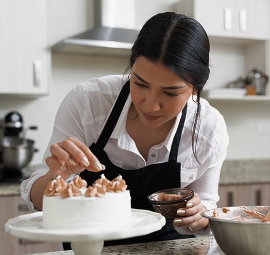Pastelera que decora un pastel con crema en su cocina