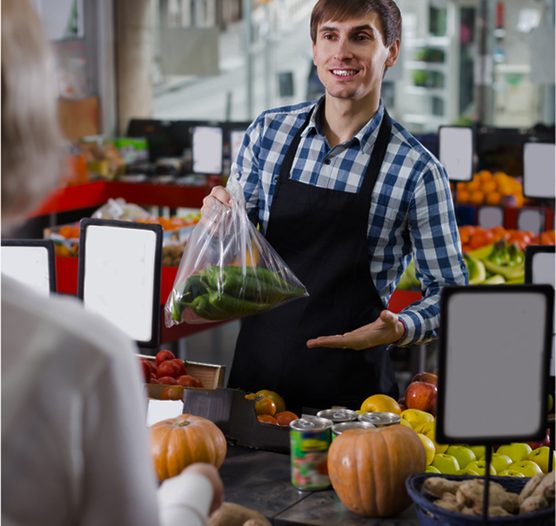 Vendedor de una tienda de verduras que entrega una bolsa a una clienta