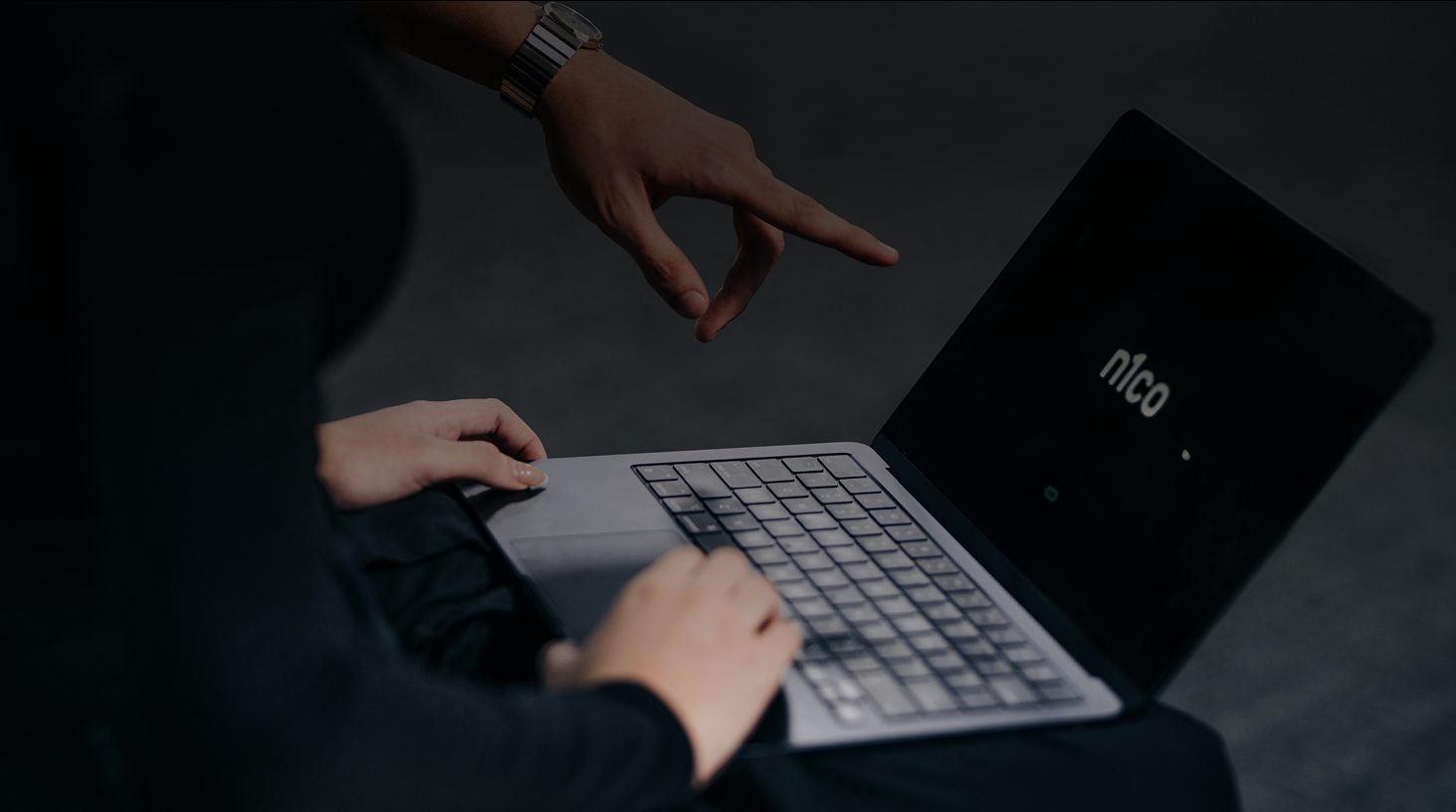 Persona que trabaja en una laptop con el logo de n1co mientras otra señala la pantalla