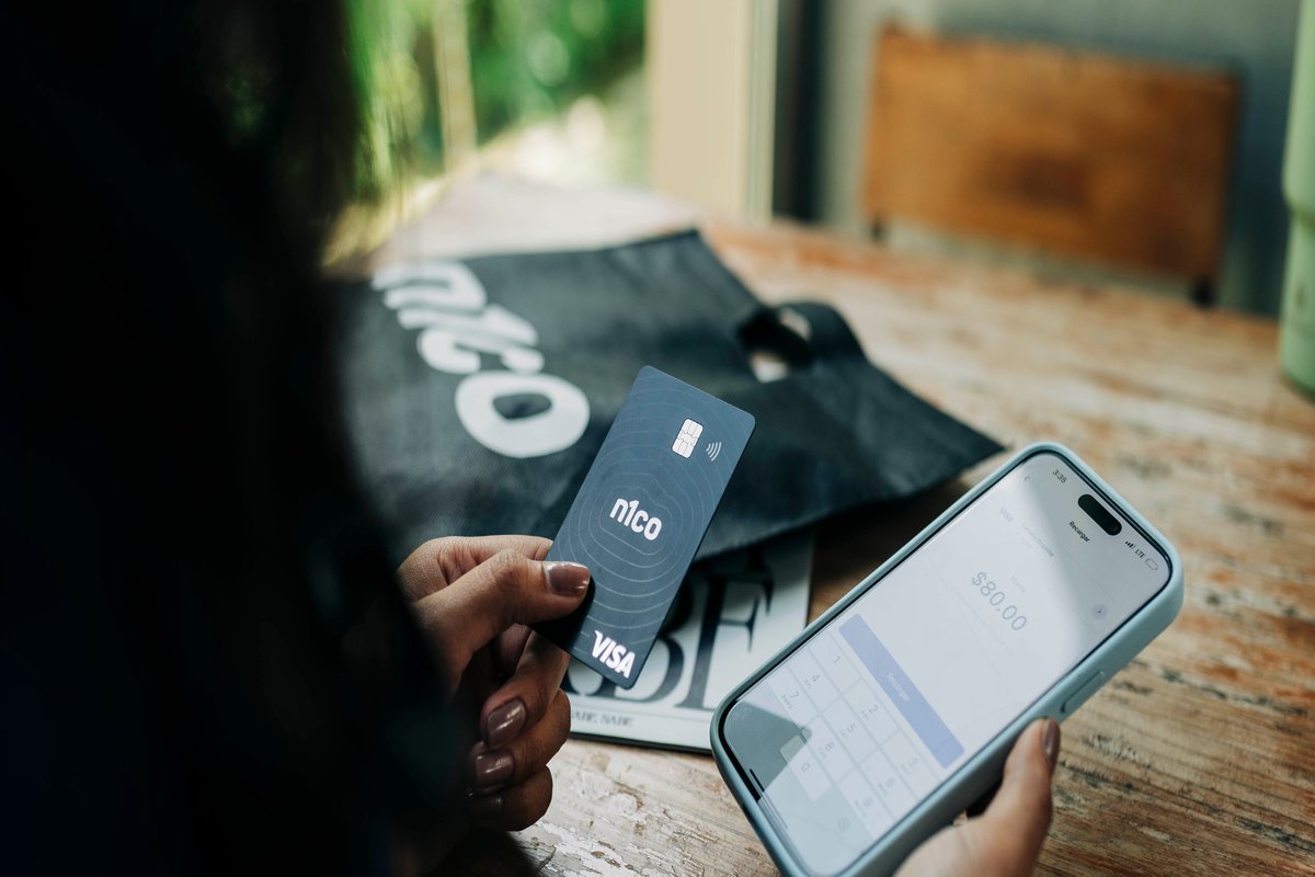 Mano que sostiene una tarjeta n1co junto a un teléfono con la app abierta
