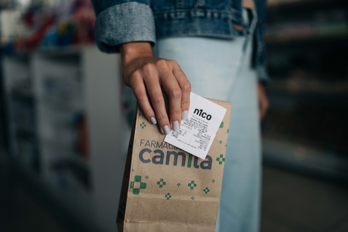 Mano que pega un recibo de n1co en una bolsa de papel de farmacia