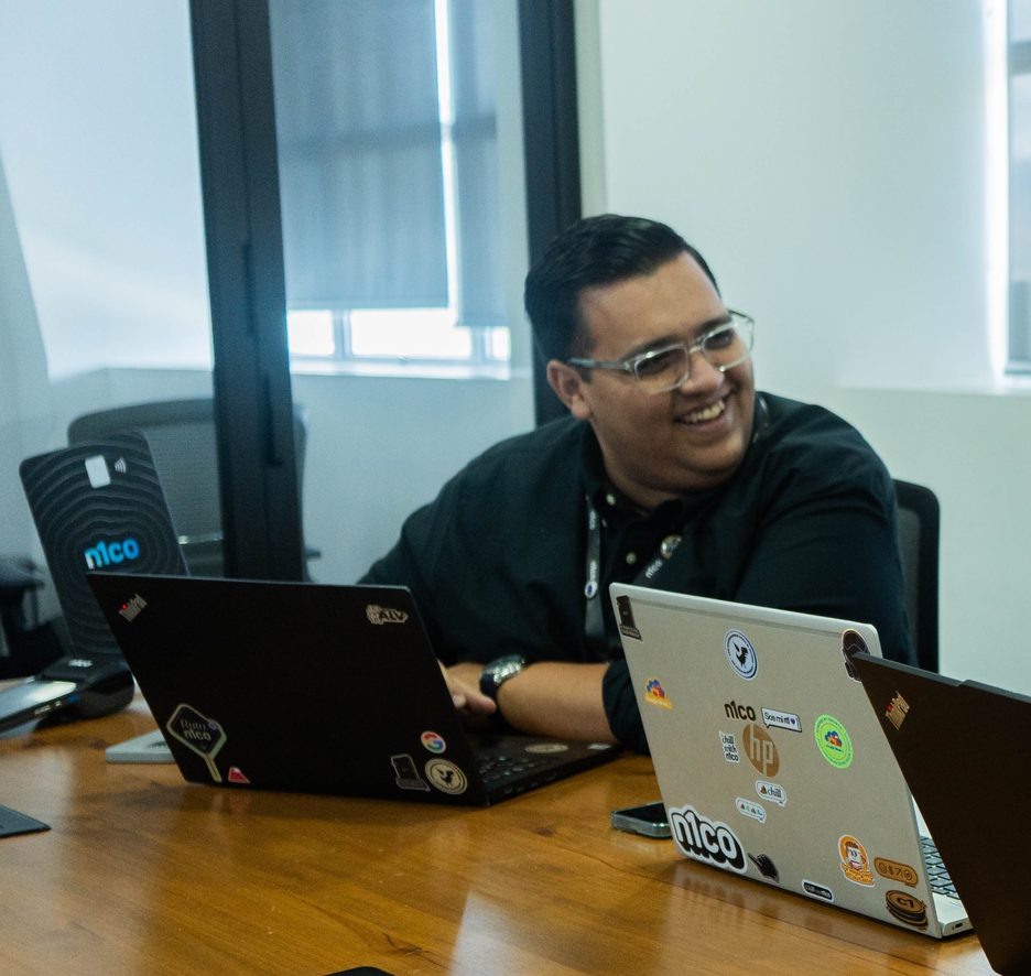 Persona del equipo de n1co sonriendo en una reunión, frente a su computadora
